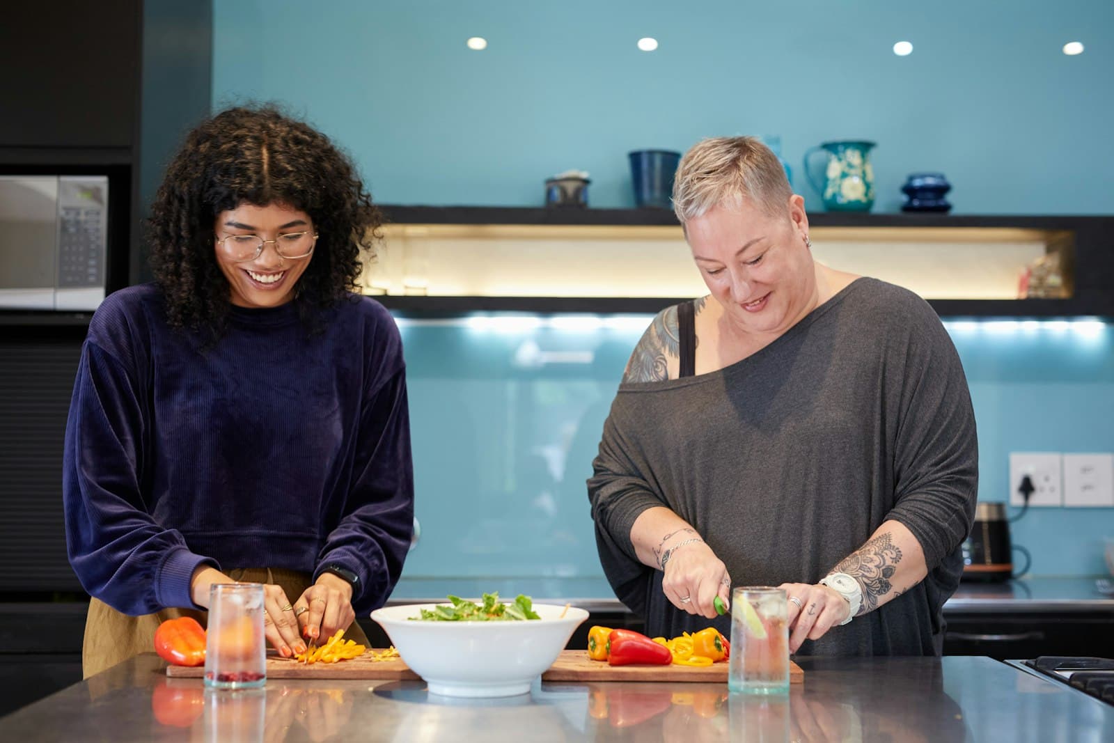 Two friends laughing while chopping vegetables together at home